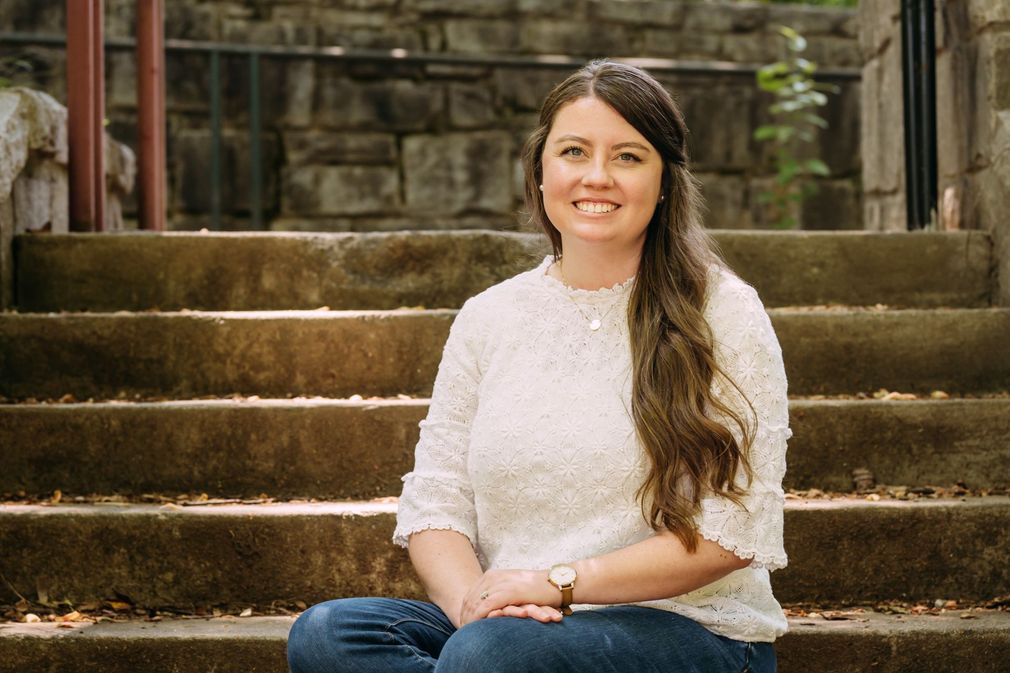 A woman is sitting on a set of stairs with her legs crossed and smiling.