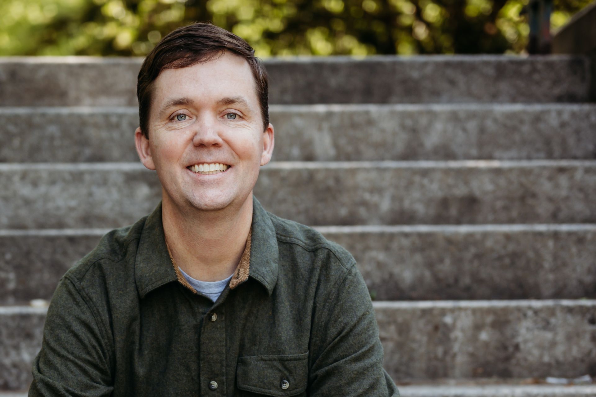 A man in a green shirt is sitting on a set of stairs and smiling.