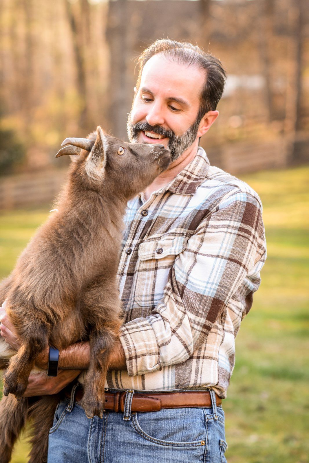 A man is holding a baby goat in his arms.