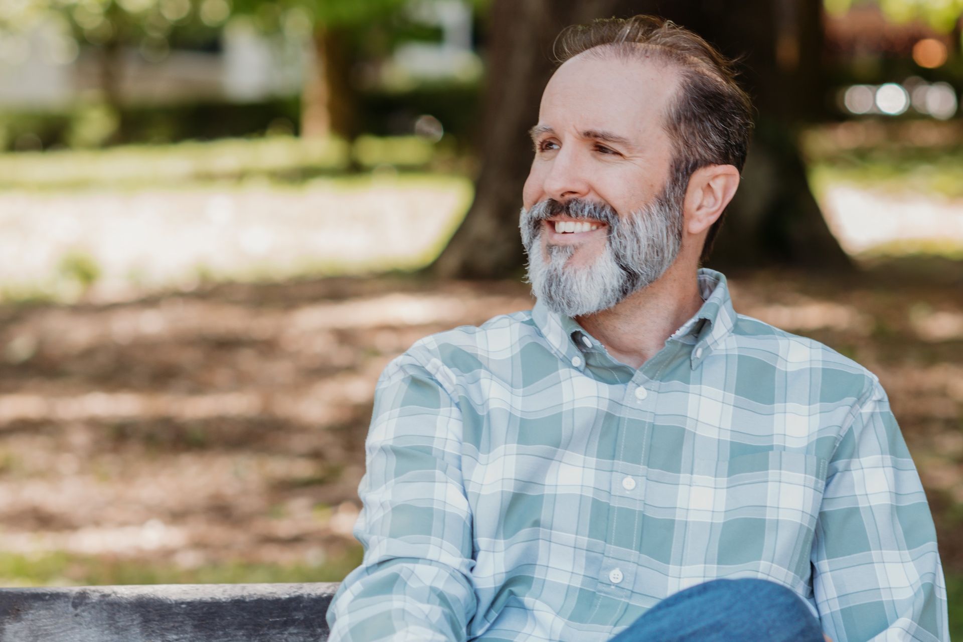 A man with a beard is sitting on a park bench and smiling.