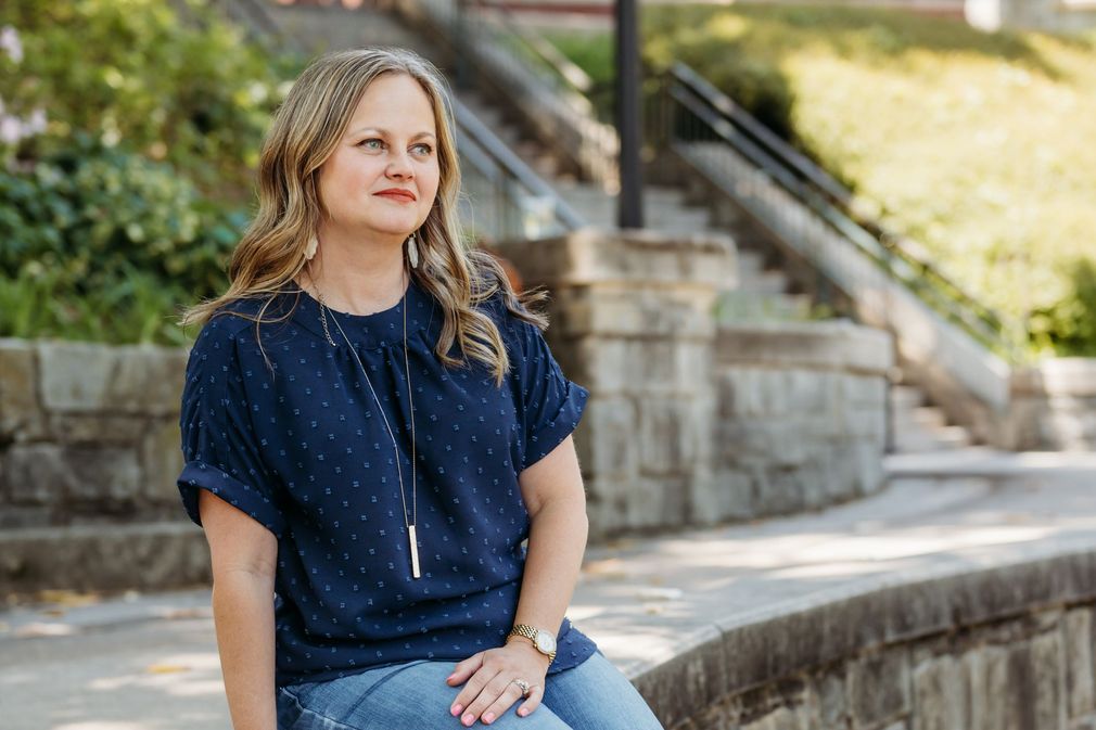 A woman in a blue shirt and jeans is sitting on a stone wall.