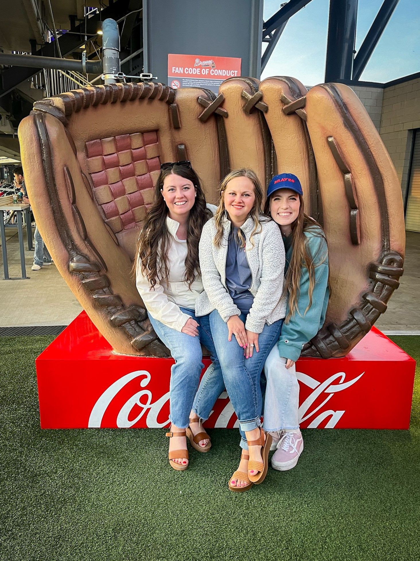 Three girls are sitting on a giant baseball glove.