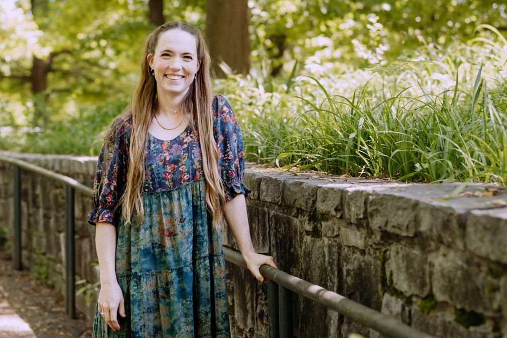 A woman in a blue dress is standing next to a stone wall.