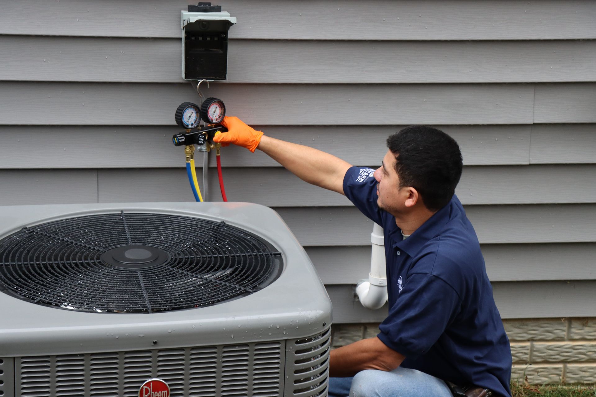 Person connecting pipes to an air conditioning unit outside, using a gauge.