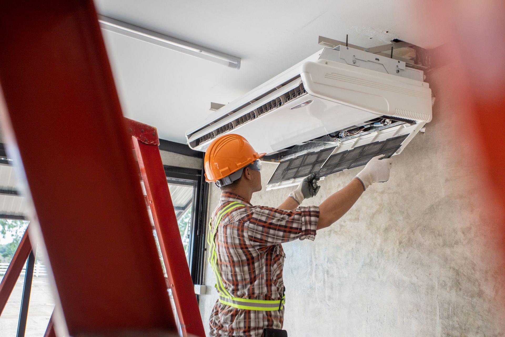 Technician wearing a hard hat servicing a ceiling mounted air conditioning unit indoors. Technician wearing a hard hat servicing a ceiling mounted air conditioning unit indoors.