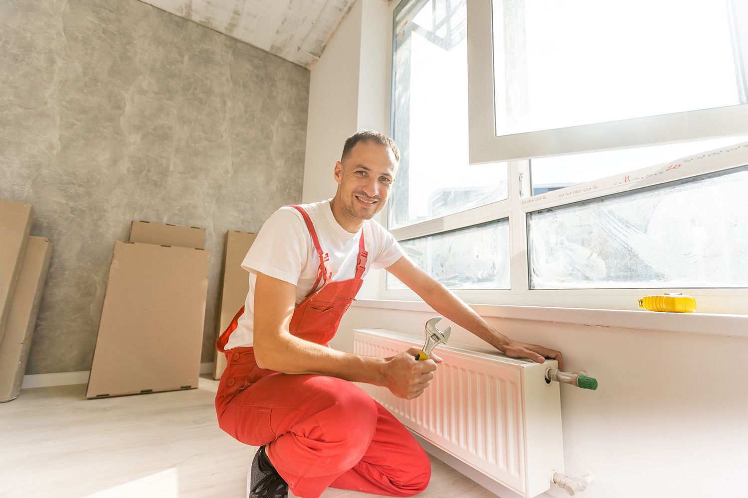 Smiling local heating contractor holding a wrench while working on a home heating system.