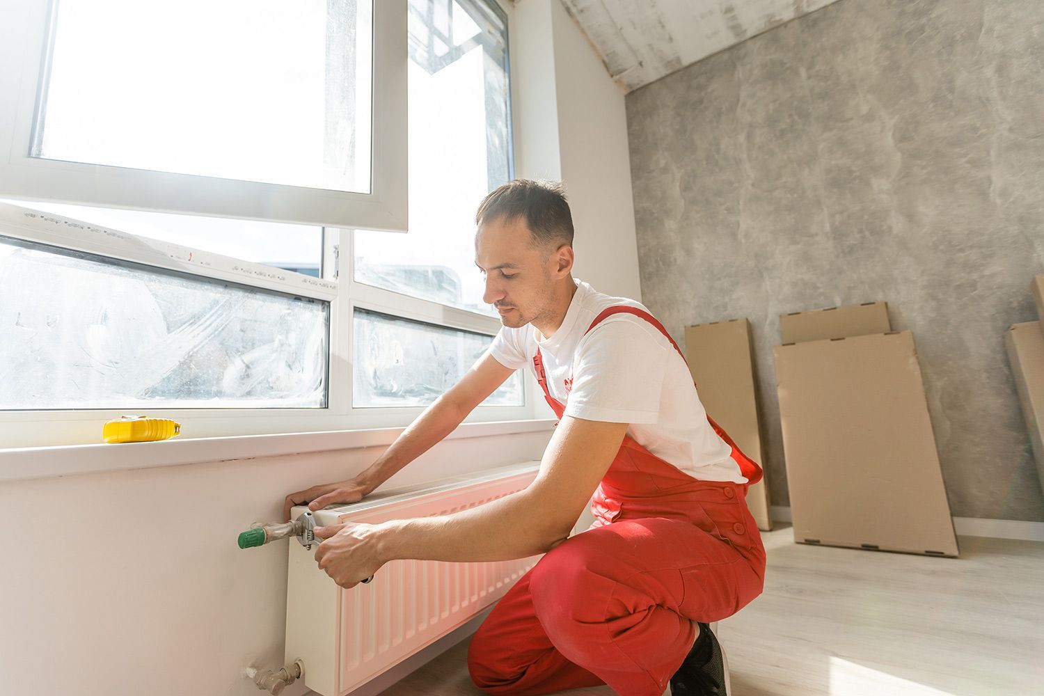 A professional local heating contractor installing a modern radiator unit in a bright room.