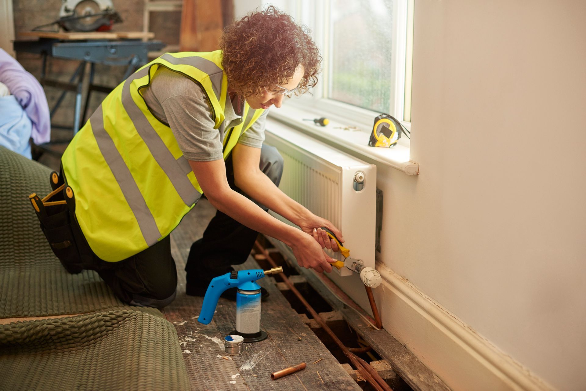 Technician repairing home radiator and plumbing lines with tools near window for heating service.
