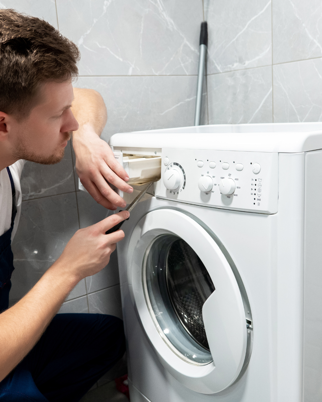 Un technicien de réparation en uniforme blanc ouvre le tiroir à lessive pendant qu'il effectue l'entretien d'une machine à laver blanche.