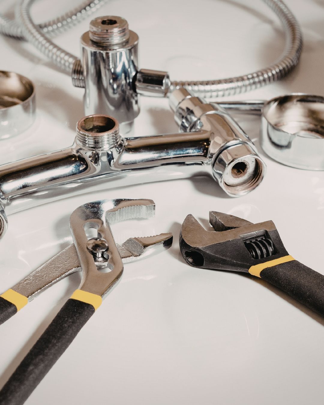 Des outils de plomberie, notamment une pince et une clé réglable, disposés à côté de composants de robinet chromés démontés.