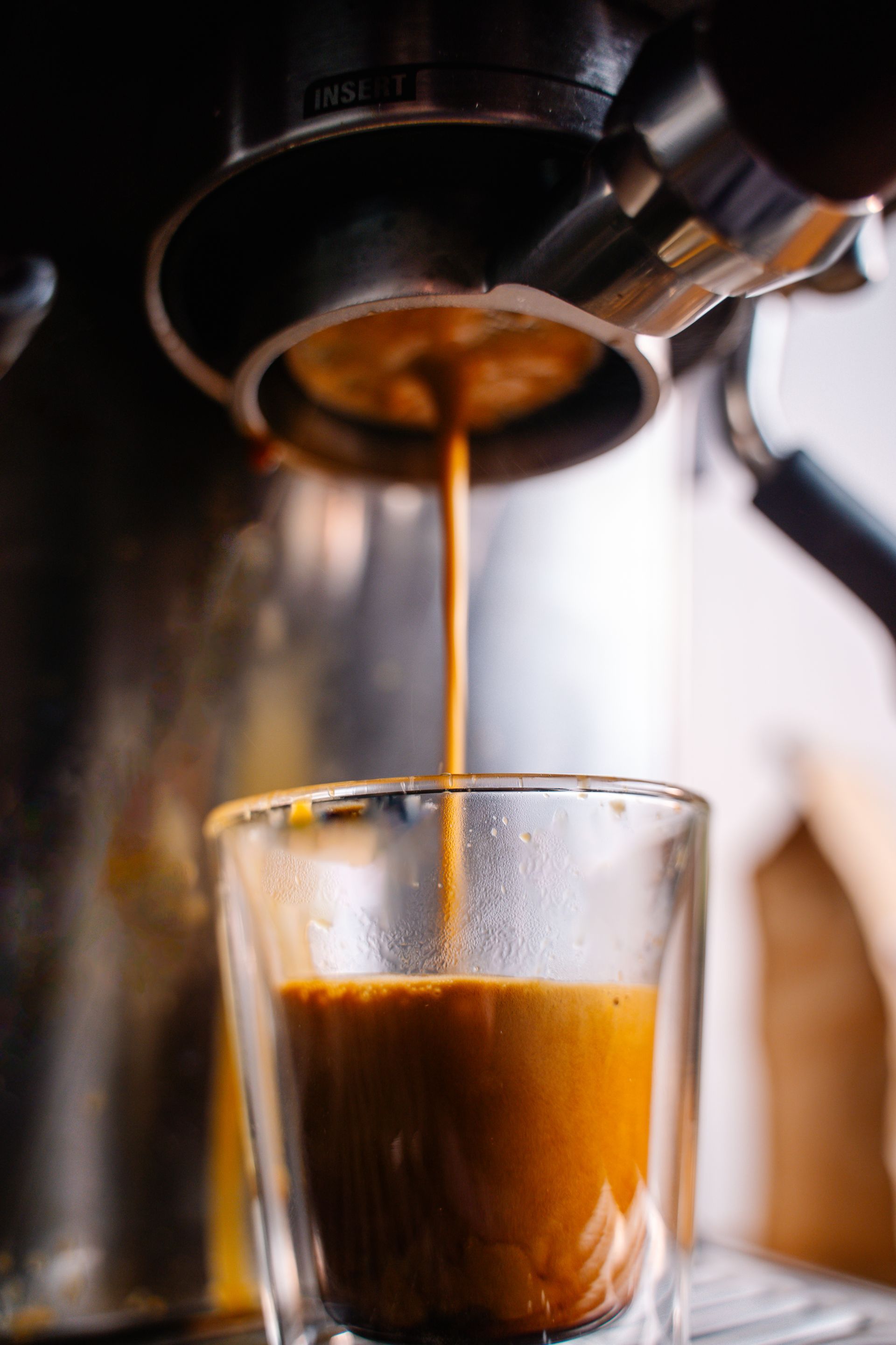 A cup of coffee is being poured from a coffee machine into a glass.