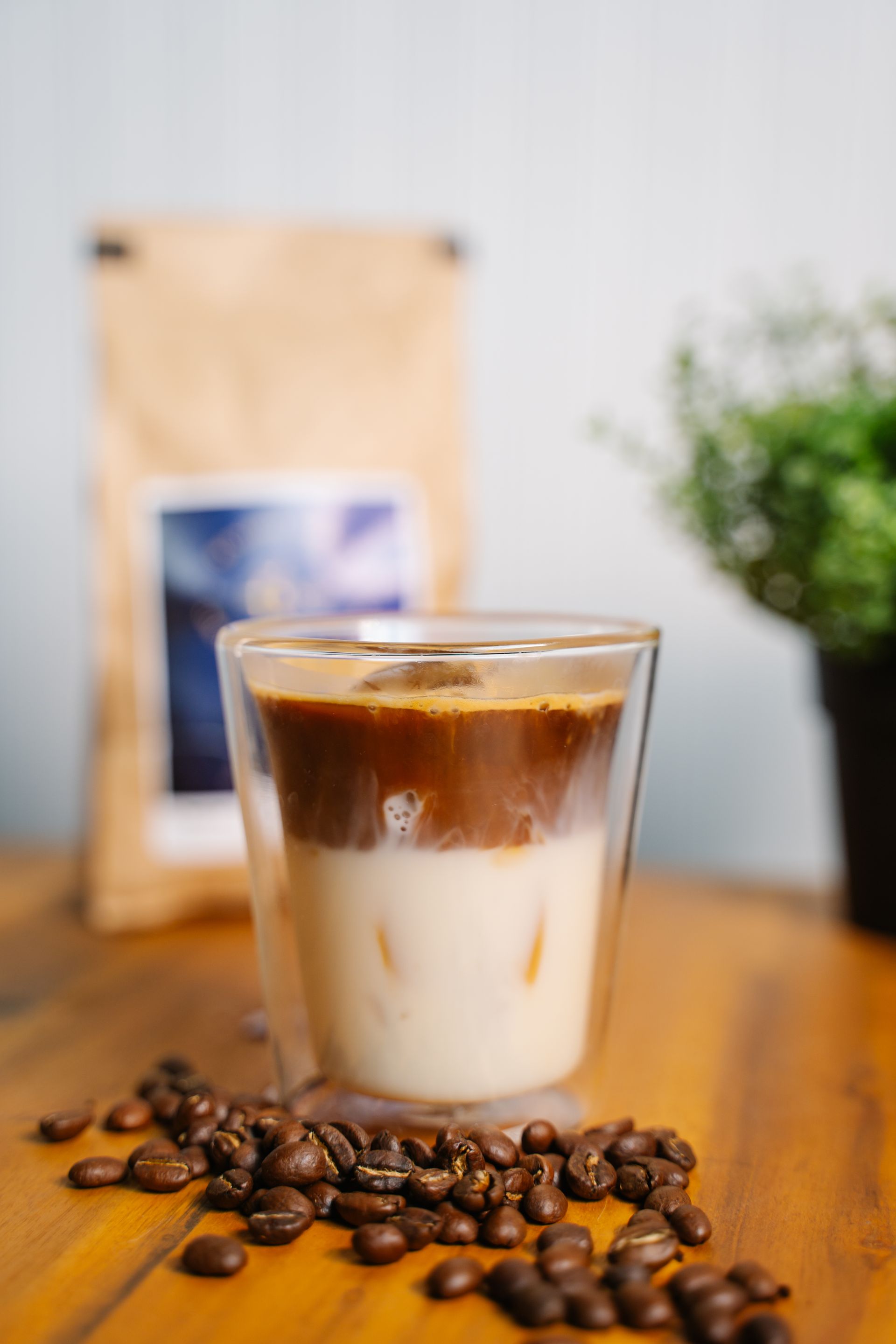 A glass of iced coffee with a bag of coffee beans in the background