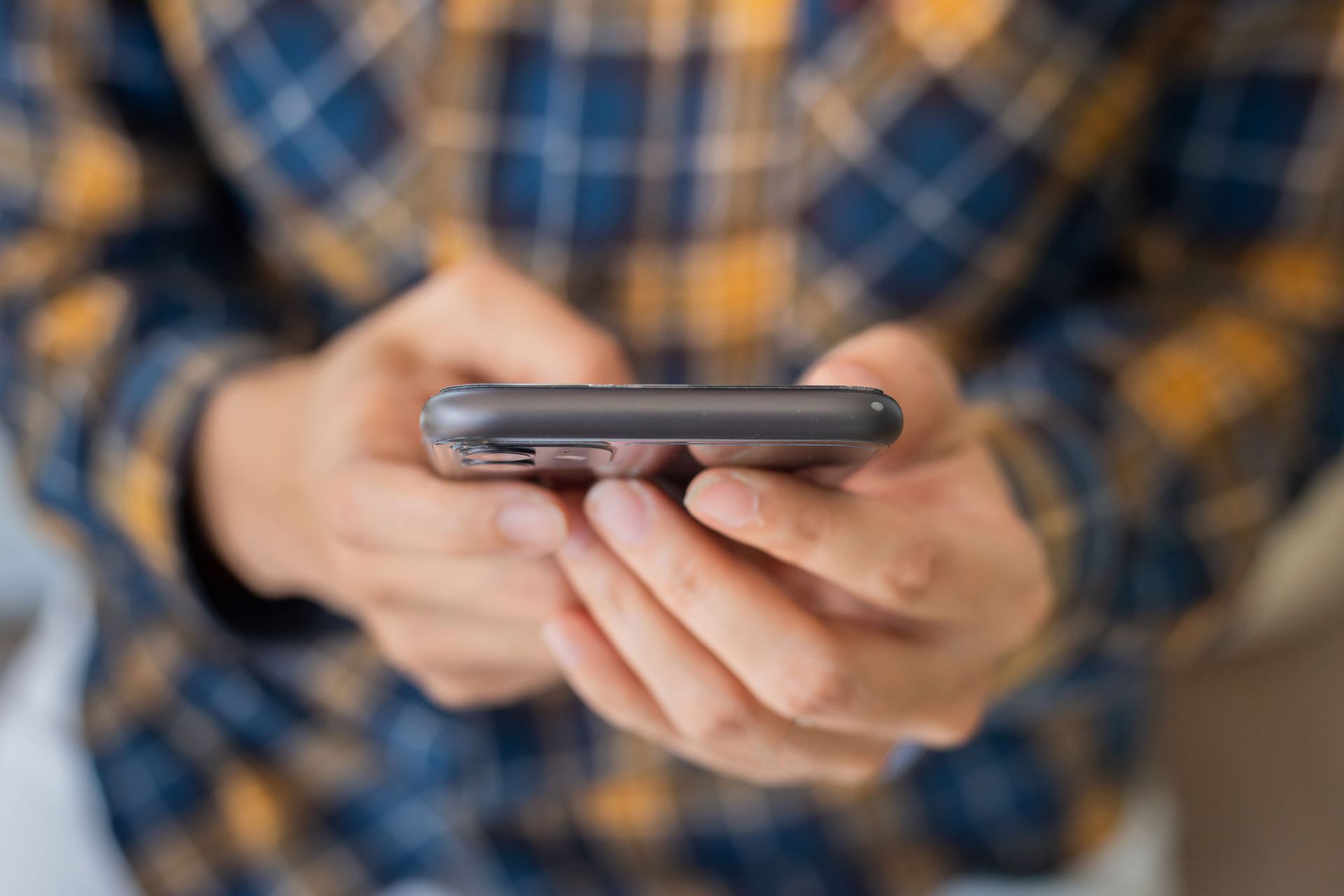 hands of male wearing plaid shirt holding phone