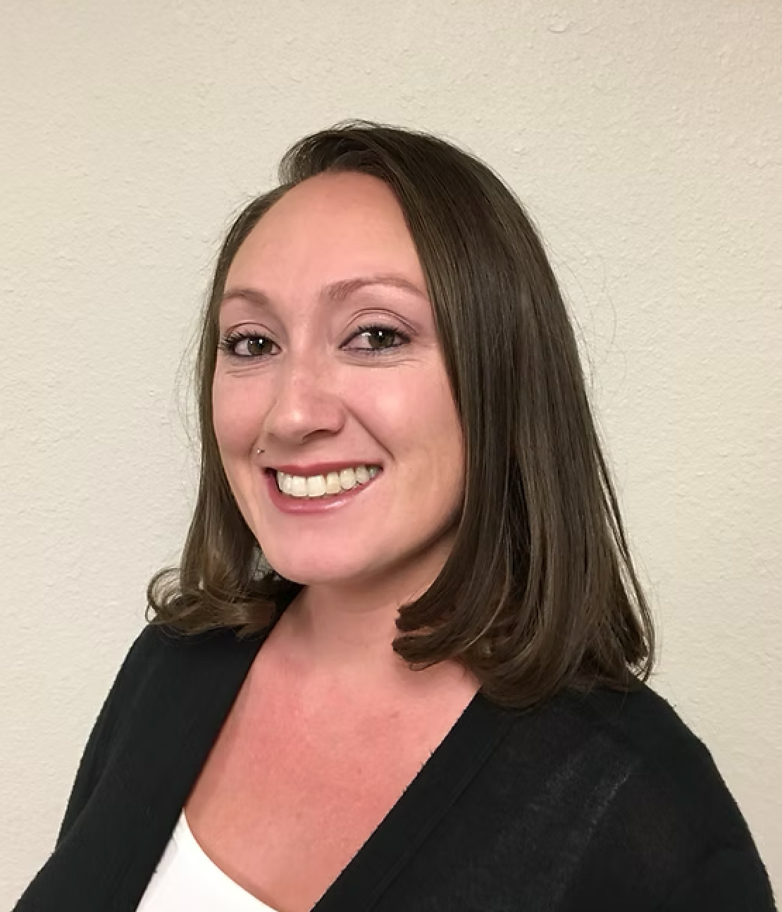A woman wearing a black sweater and a white shirt is smiling for the camera.