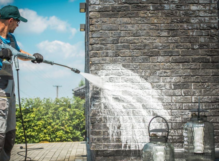 A man is cleaning a brick wall with a high pressure washer.