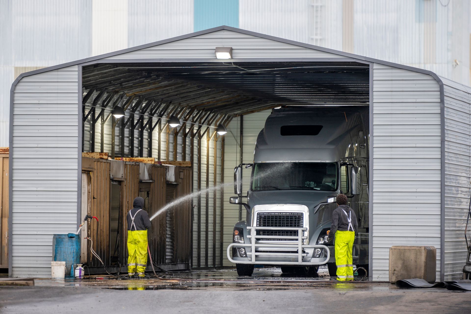 Two men are washing a semi truck in a garage.