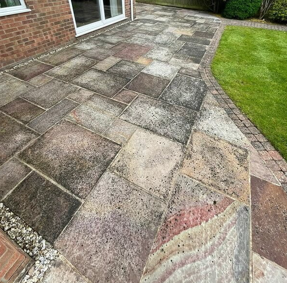 Patio of multi-colored stone bricks, adjacent to a lawn and building entrance.