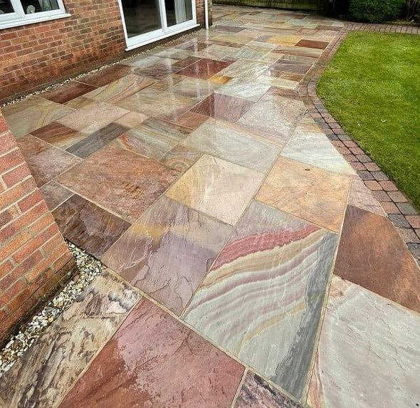 Multi-colored stone patio next to a red brick house and lawn.