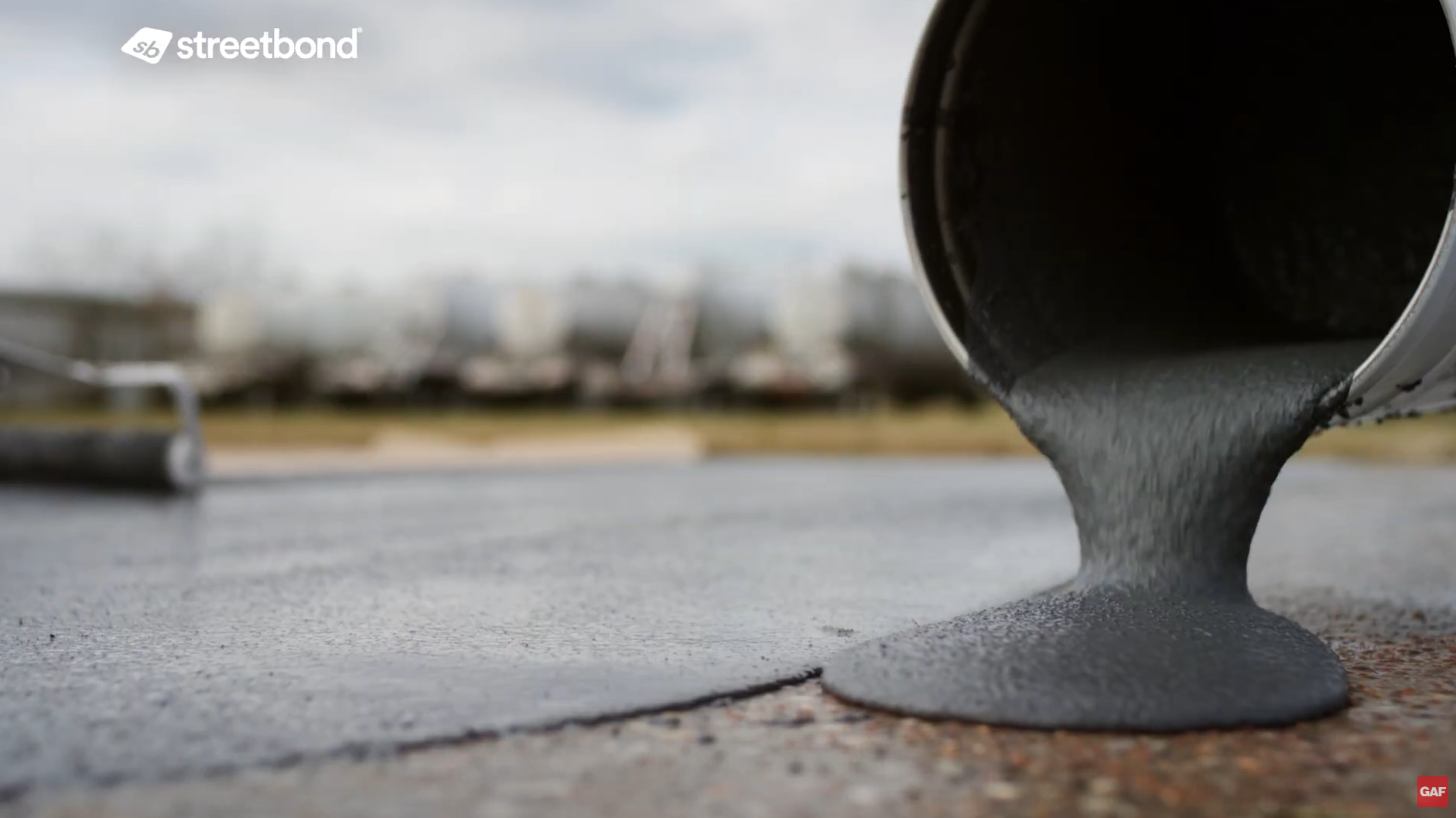Gray liquid concrete pouring from a metal container onto a paved surface outdoors.