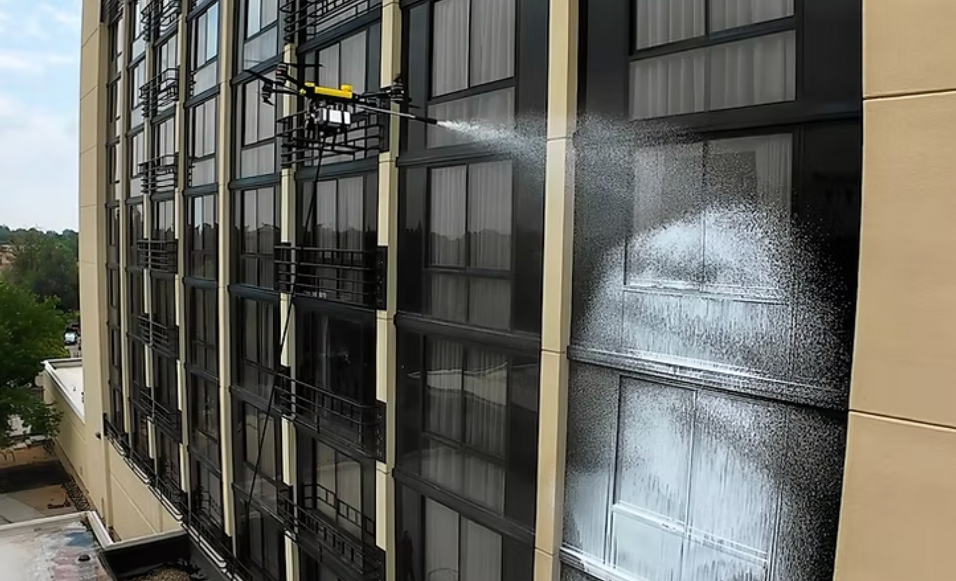 A drone sprays cleaning foam onto the glass exterior of a high-rise building.