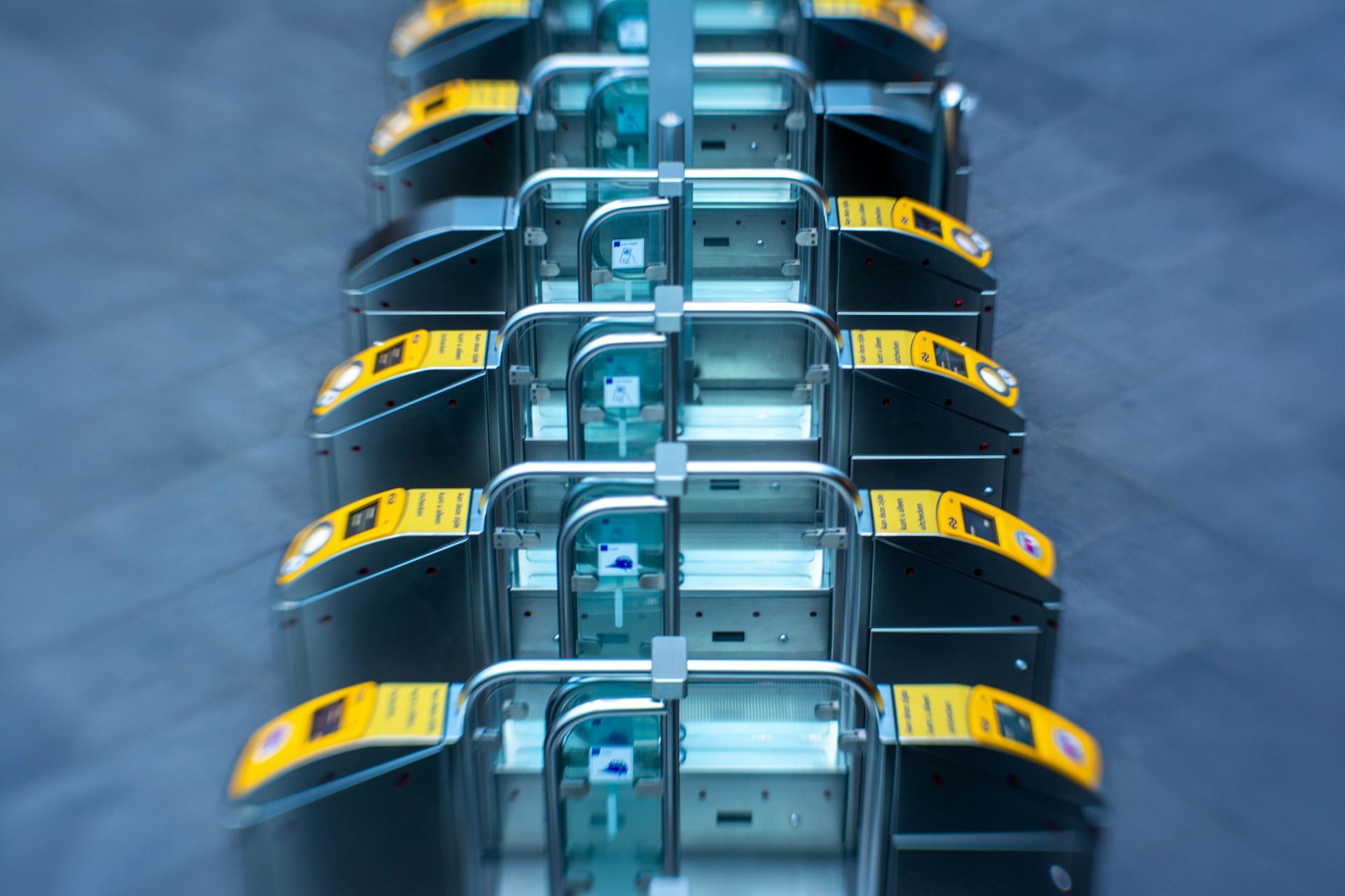 A row of subway turnstiles with yellow card readers and silver handles.