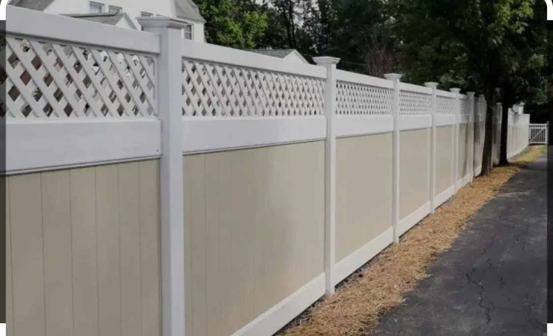 A long, white vinyl fence with a lattice top and tan panels, bordering a paved road.