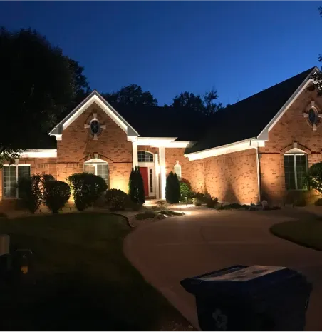 Brick house at dusk with warm exterior lighting and a curved driveway.