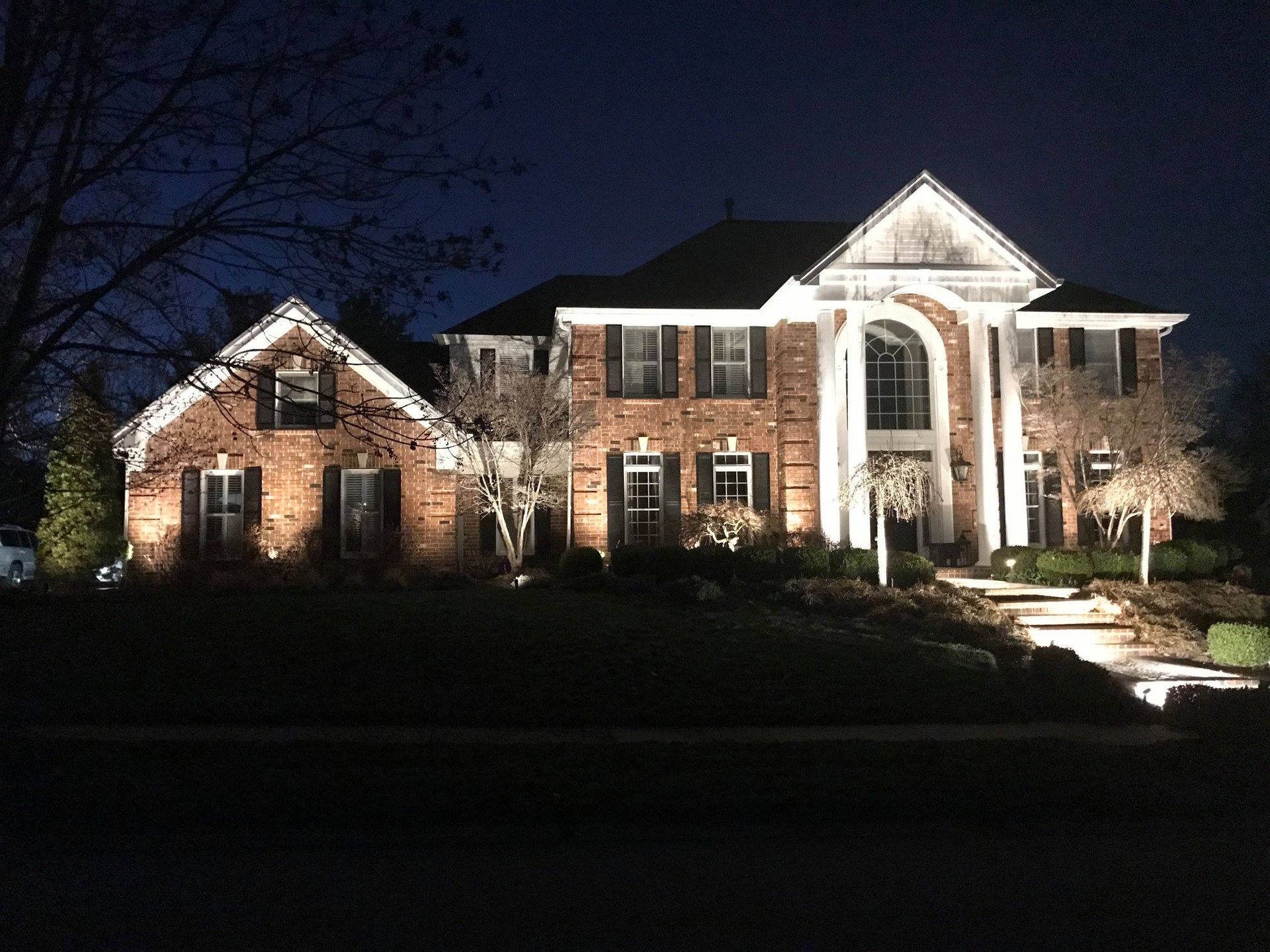 Large brick house lit up at night, with white columns and a front walkway in the yard