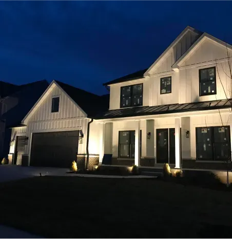 Modern two-story house exterior at night, lit by warm porch lights against a dark blue sky.