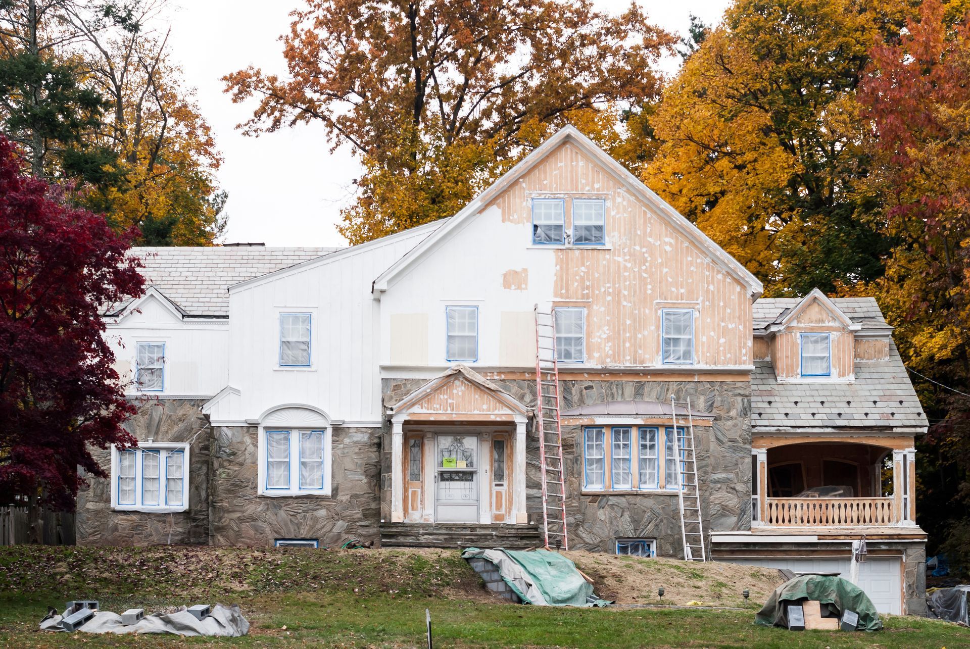 House undergoing renovation with stone and white siding, fall foliage.