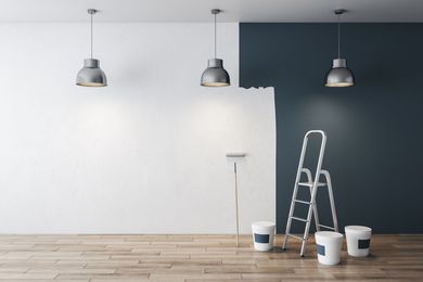A room being painted with a white wall and a dark blue wall. A ladder, paint buckets, and a roller are present.