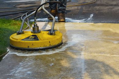 Person using a yellow surface cleaner to wash a concrete driveway.