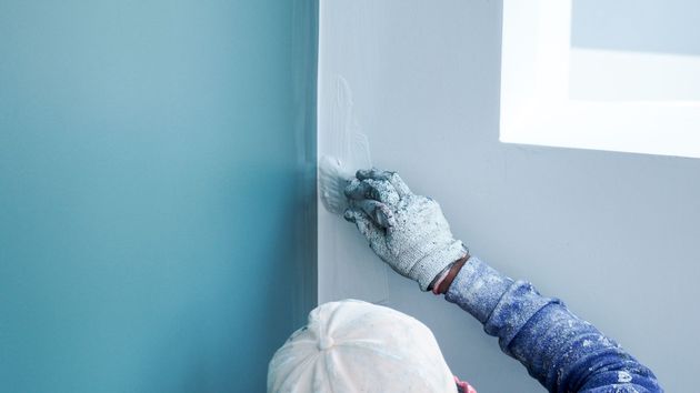 Person in paint-covered gloves smoothing putty into a wall corner, next to blue paint.
