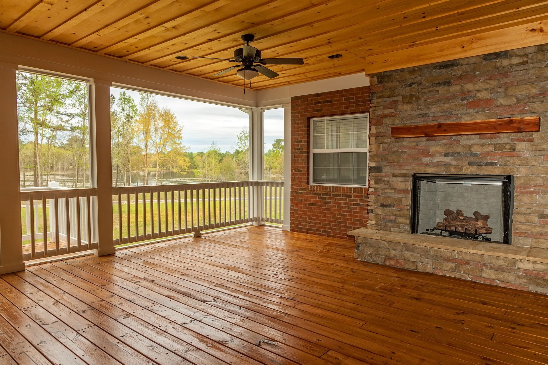 Covered porch with fireplace, wooden ceiling and floor, overlooking a body of water.