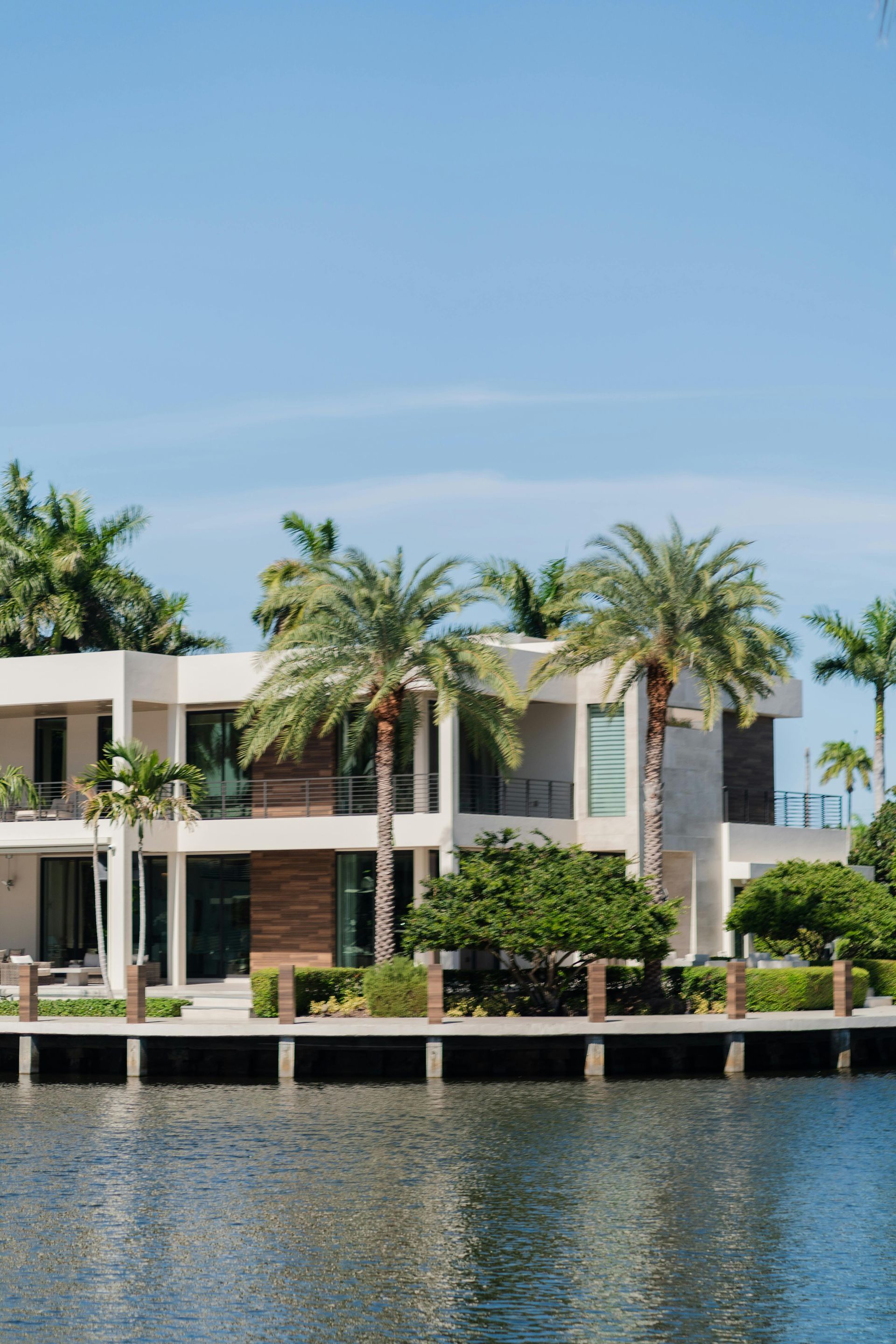 Modern waterfront home with palm trees against a blue sky.