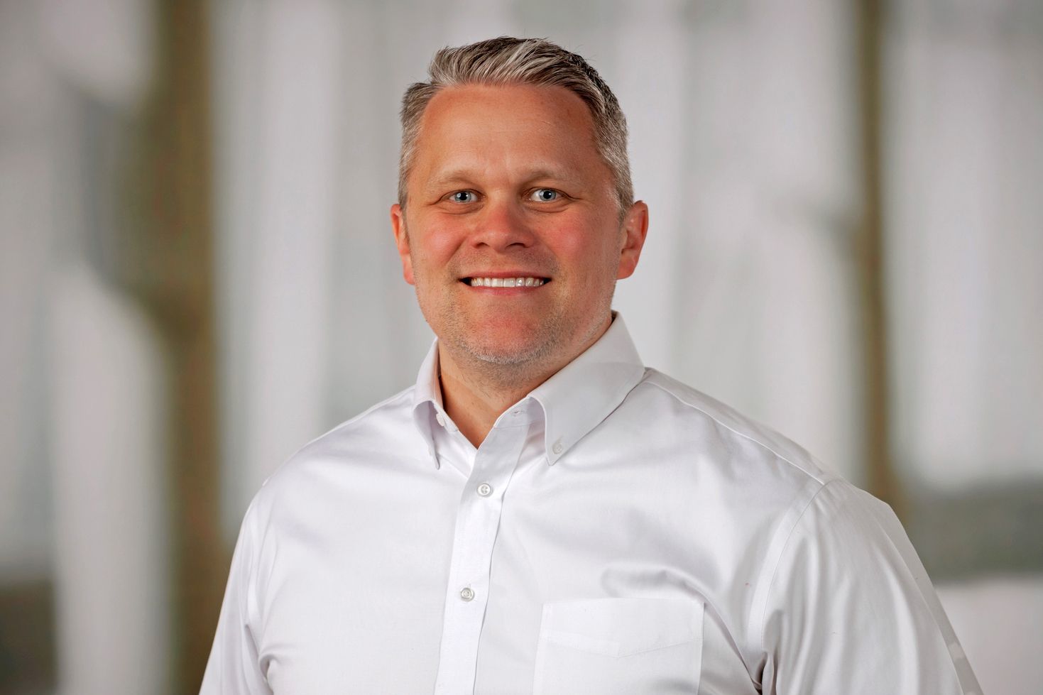 Smiling man with graying hair in a white shirt, office setting.
