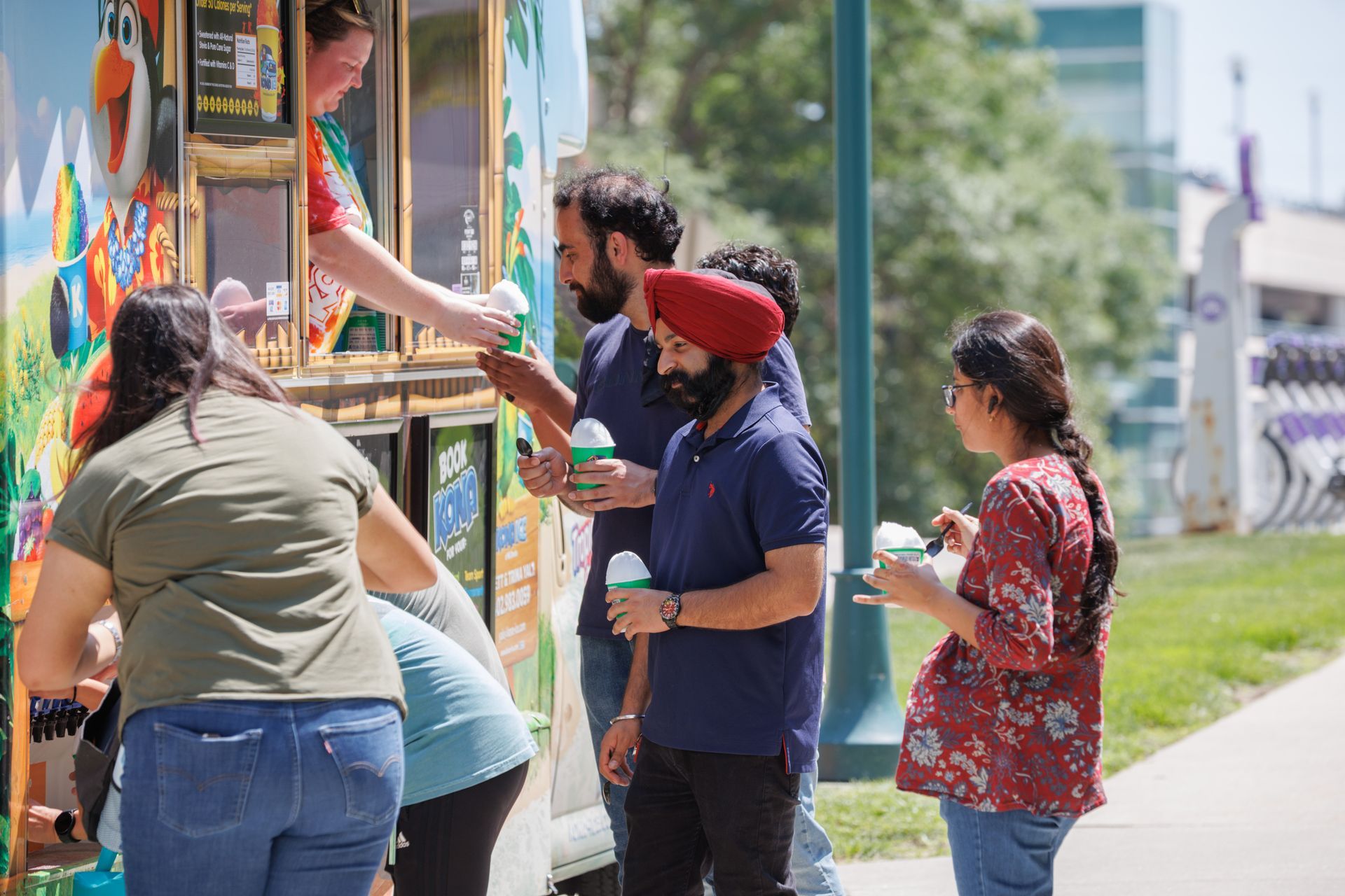 People buying shaved ice from a food truck on a sunny day.