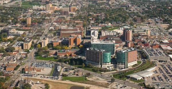 Aerial view of a city with tall buildings, some reddish-brown and others glass-fronted, on a sunny day.