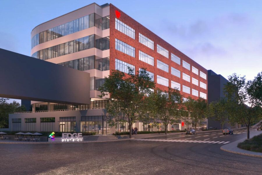 Modern brick and glass office building, with a connecting bridge, trees, and a blue, purple, and green sign.