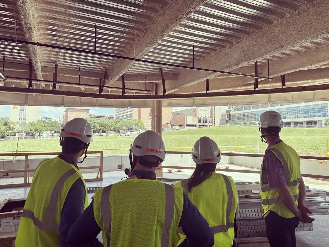 Construction workers in hard hats and vests looking out at a stadium.