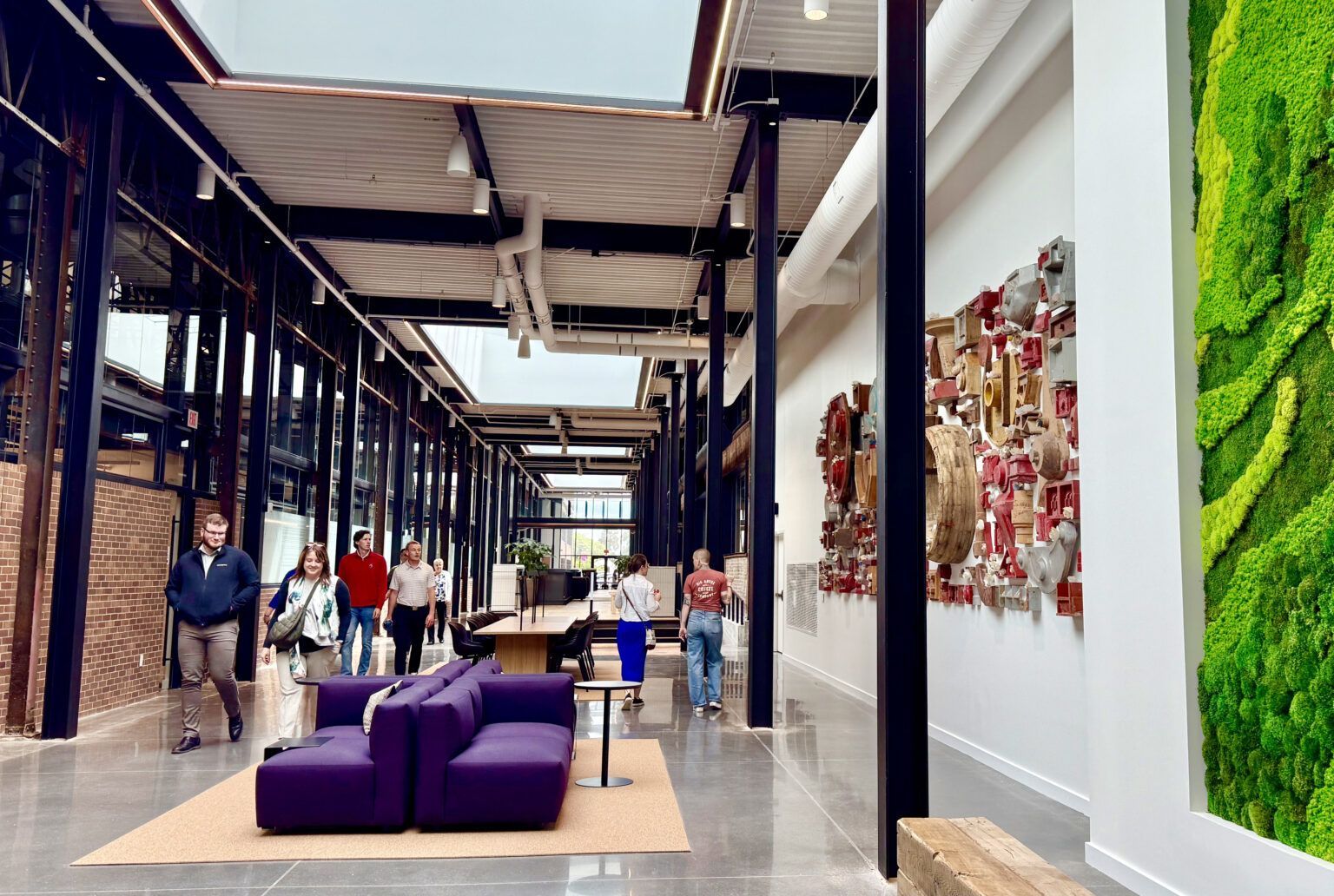 People walking through a modern office hallway. Purple couch, art, and a vertical garden.