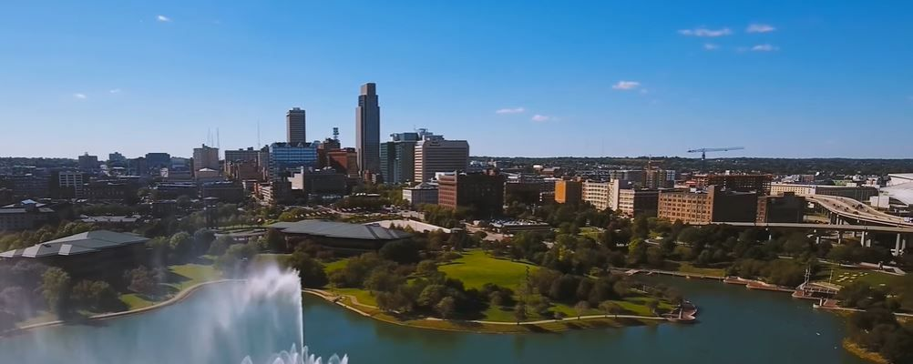 Aerial view of Omaha, Nebraska skyline with fountain in foreground and blue sky.