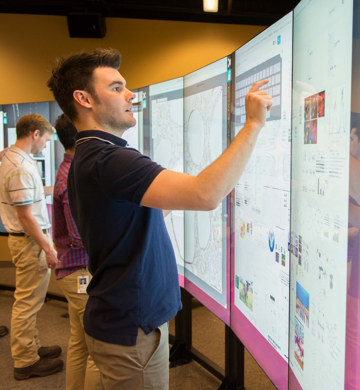 Man interacts with large touch screen displays, with others looking on.