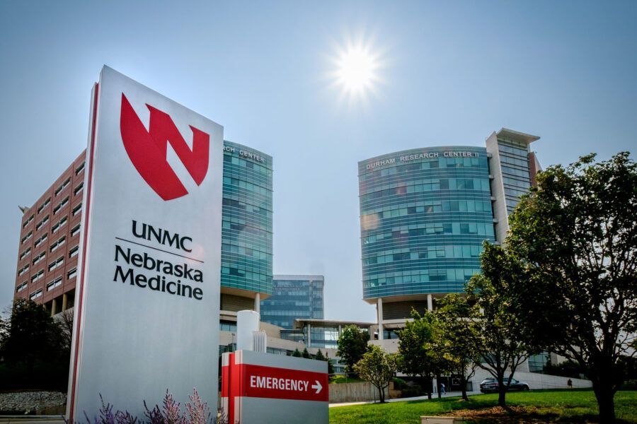UNMC Nebraska Medicine sign with hospital buildings and bright sun.