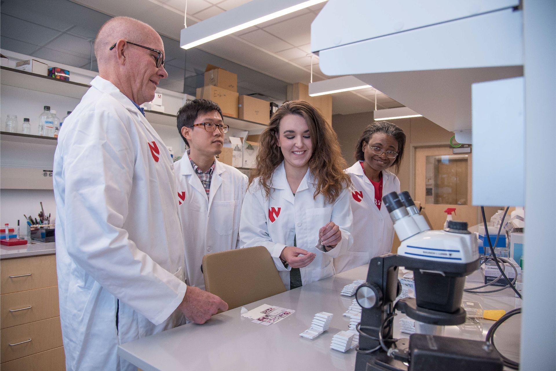 Four people in lab coats examining samples in a laboratory.