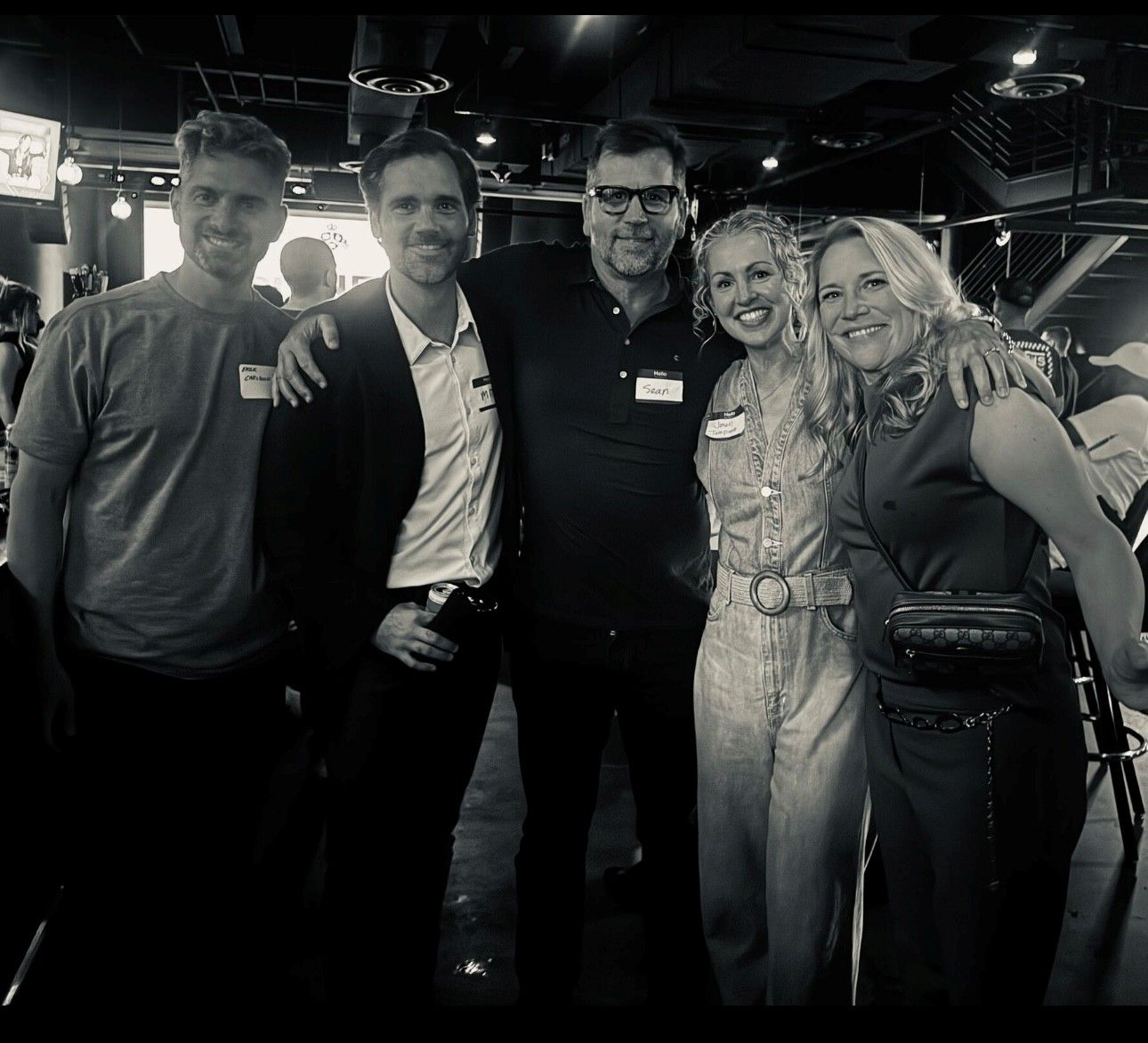 Office building with brick facade, arched windows, pedestrian bridge, trees, and signage.