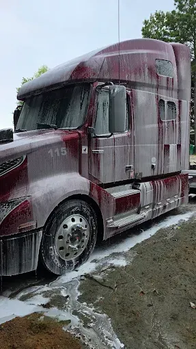 Red semi-truck covered in white foam suds, parked on dirt.
