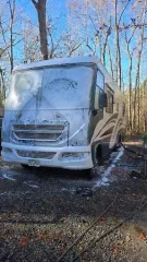 RV being washed with soapy foam outdoors; trees in background.