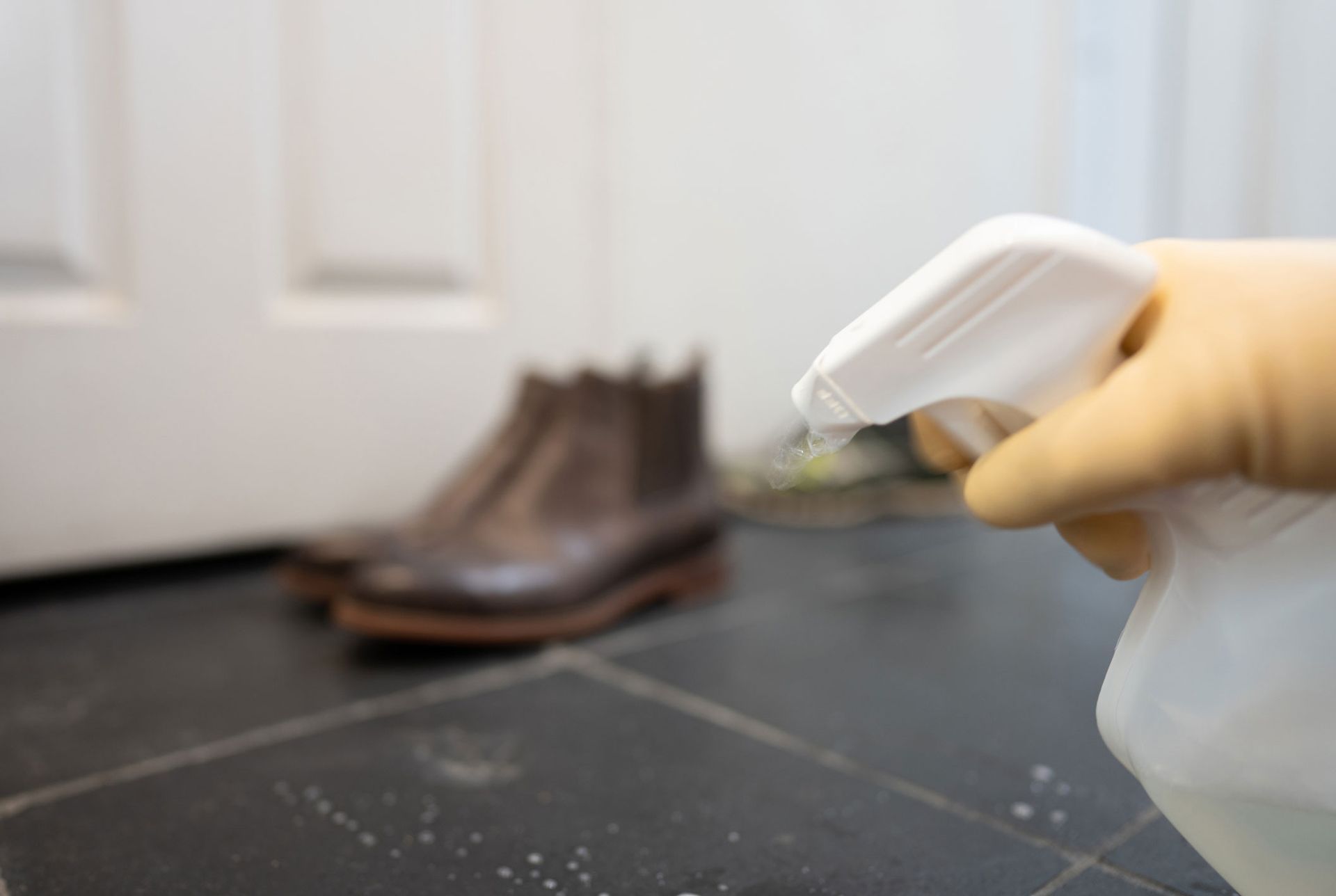 A person is spraying a bottle of cleaner on a tiled floor.