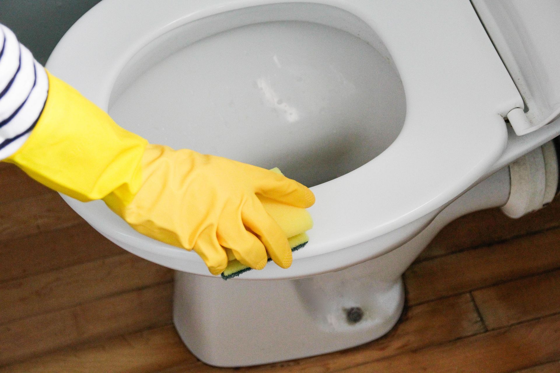 A person wearing yellow gloves is cleaning a toilet with a sponge.